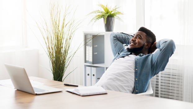 Daydreaming. Cheerful african american employee leaning back on chair with hands behind head, resting at workplace in modern office photo