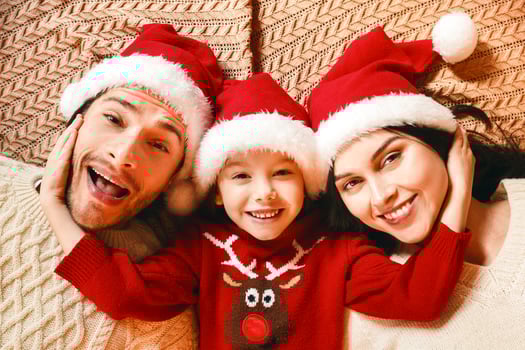 Top view of young happy family in santa hats laying down on bed or floor, little girl embracing parents, happy family concept photo