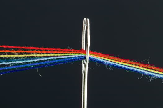 multi-colored threads for sewing in the form of a rainbow pass through an antique needle on a black background photo