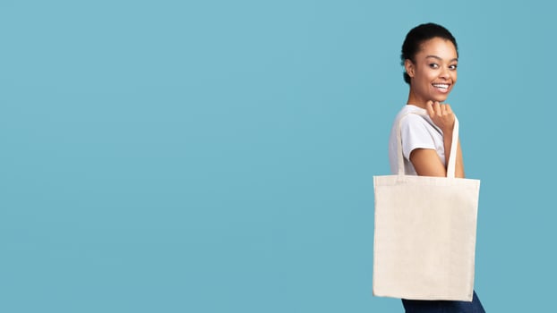 Eco Bag. Afro Woman Holding White Blank Canvas Tote Handbag Shopper Standing Over Turquoise Studio Background. Panorama, Free Space photo