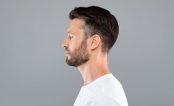 Side view of middle-aged bearded man in white t-shirt over grey studio background, copy space. Profile portrait of handsome man with closed eyes posing on gray, standing straight and looking aside photo