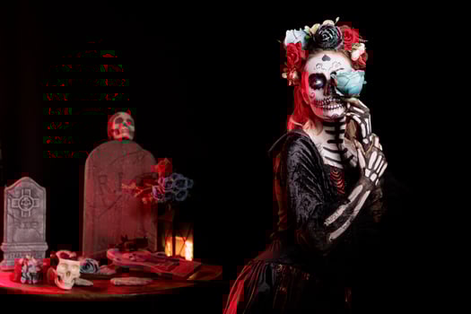 Sensual woman posing with blue rose for Day of the Dead Mexican celebration honoring dead loved ones. Seductive girl doing ancient Aztec custom of celebrating ancestors, wearing skull face paint photo