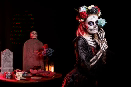 Woman doing sensual pose with rose in graveyard, celebrating Dia de los Muertos. Peculiar girl holding flower surrounded by frightening funeral items during Halloween horror event photo