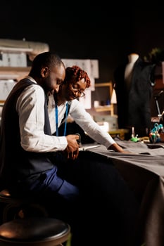Experienced suitmakers manufacturing bespoke sartorial clothing in upscale atelier studio. Skilled fashion designers meticulously cutting fabric material for customer comissioned stylish outfit photo