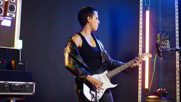 Woman performer showing thumbs up symbol and playing guitar, edgy grunge music performance in studio. Female rocker artist giving her approval with a positive like sign. Camera A. photo