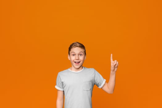 Emotional teen boy having idea, pointing finger up, got problem solution, orange studio background photo