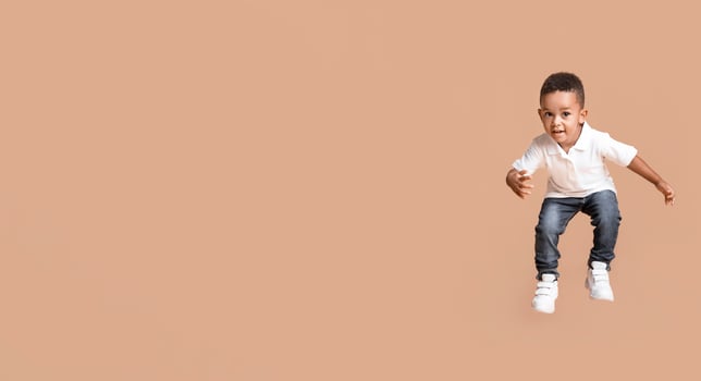 Adorable afro baby boy jumping over yellow studio background with copy space photo