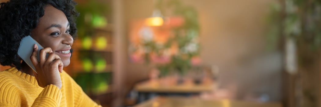Side view of young african american young woman talking by modern smartphone, cafe interior, close up, panorama with copy space photo