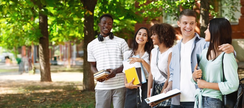 Group of international students standing together outdoors in college campus, chatting and laughing, free space photo