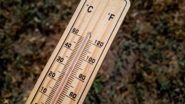 Close up of a wooden thermometer on dry grass indicating extreme heat, relating to summer and climate change awareness photo