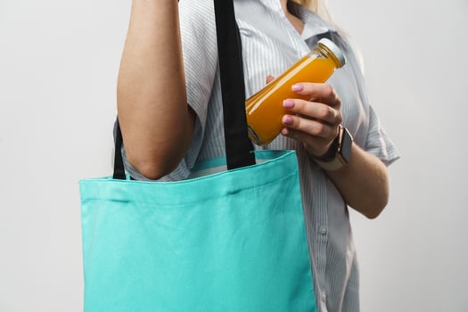 Cropped woman holding fabric shopping bag and juice bottle, studio shot photo