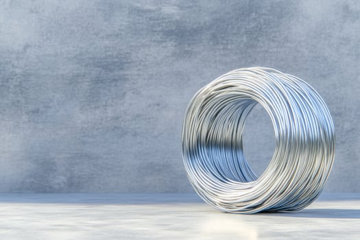 A tightly coiled roll of silver metal wire placed on a smooth concrete surface, reflecting soft light. photo