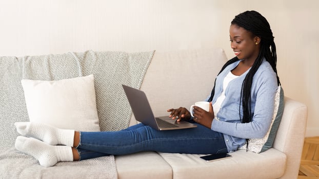 Modern Job Search. Smiling Black Woman Using Laptop Browsing Work Opportunities Online While Sitting On Couch With Coffee At Home, Free Space photo