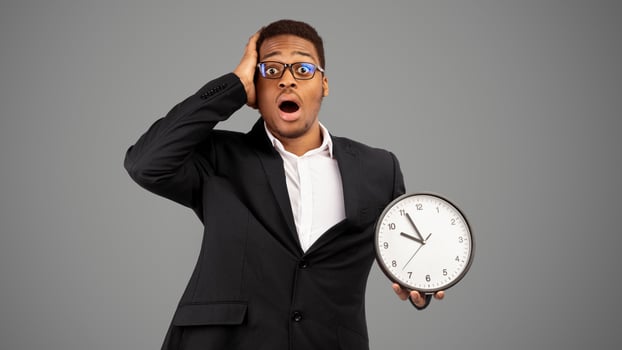 Time Management Concept. Shocked black man holding wall clock, running out of time, white background. Panorama photo