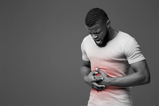 Young afro guy suffering from stomach ulcer, touching his tummy over white background, copy space photo