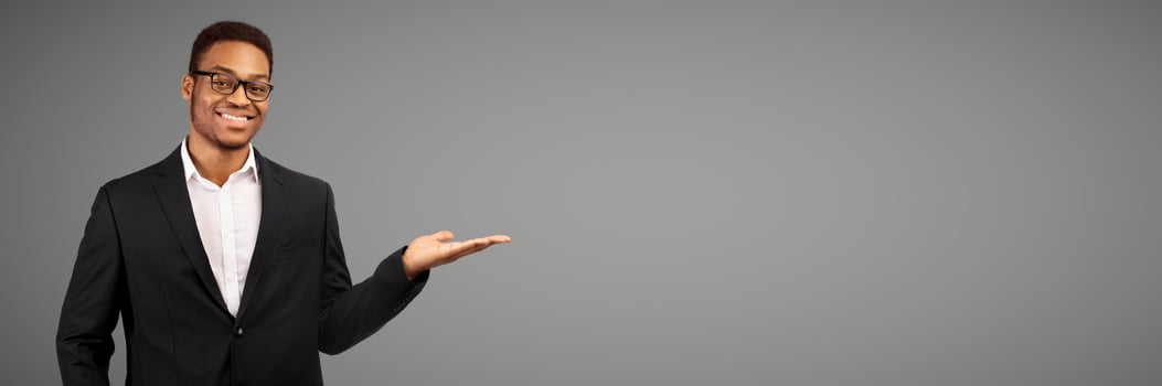 Buy This. Happy afro businessman holding invisible object on his palm, white studio wall, copyspace, panorama photo