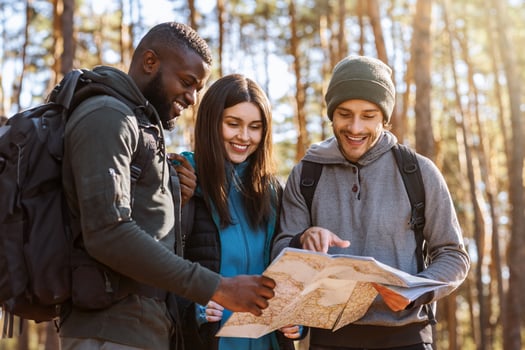 Multiracial friends with backpacks looking at map, hiking in autumn forest photo