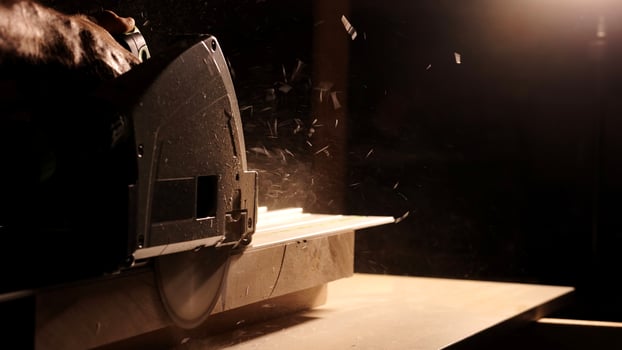 Close-up of a man cuts a wooden plank with an electric circular saw in a workshop. Cutting a piece of wood on a circular saw in backlight. Ideal topics related carpentry, efficient sawing techniques photo
