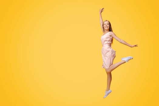 Full Length Portrait Of Joyful Teen Girl In Summer Cocktail Dress Jumping High In The Air Over Yellow Background In Studio, Copy Space photo