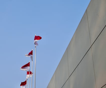 Indonesian national red and white flag. Bendera merah putih on flagpole isolated on horizontal blue sky and wall exterior background. photo