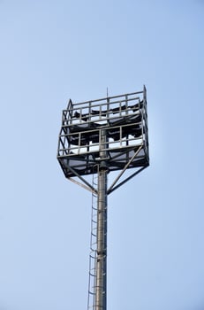 Tall floodlight stadium lamp post tall metal structure from behind view isolated on vertical blue sky background. photo