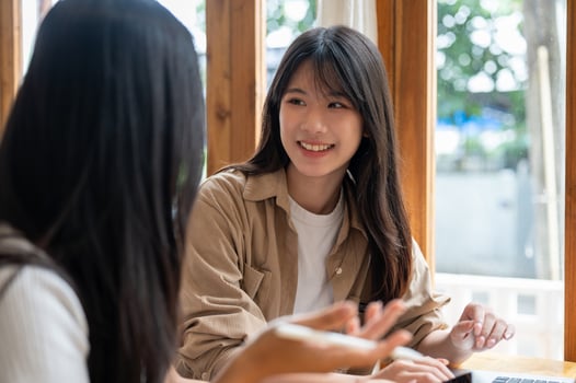 A beautiful, positive young Asian woman is chatting with her friend while meeting at a coffee shop. photo