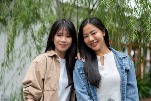 Two beautiful young Asian women in casual clothes standing in a green garden, smiling at the camera. photo
