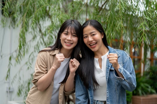 Two beautiful Asian women standing in a green garden, showing their fist and smiling at the camera. photo