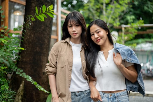 A portrait features two beautiful Asian women standing in a garden outdoors, smiling at the camera. photo