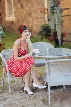 A beautiful woman in a red dress with a cup of coffee is sitting at a table in an outdoor cafe photo