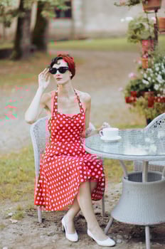 Young beautiful woman in a red dress wearing sunglasses is sitting at a table in an outdoor cafe photo