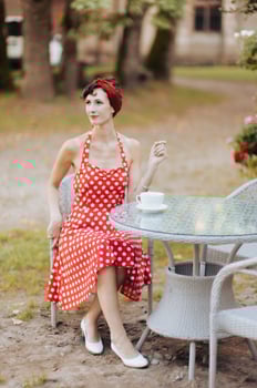 Young pretty woman in a red dress with a cup of coffee is sitting at a table in an outdoor cafe photo