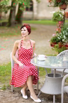 Young beautiful woman in red dress with cup of coffee is sitting at table in outdoor cafe photo