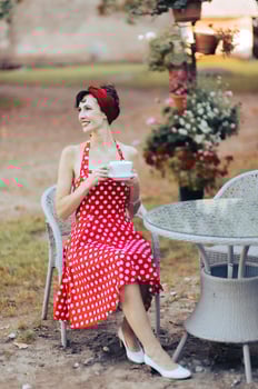 Stylish beautiful female in red dress with coffee cup sitting at a table in an outdoor cafe photo