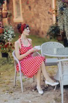 A beautiful woman in a red dress with a cup of coffee is sitting at a table in an outdoor cafe, blurred nature background photo