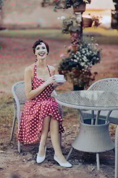 A beautiful woman in a red dress holds a cup of coffee and laughs heartily while sit at cafe table photo