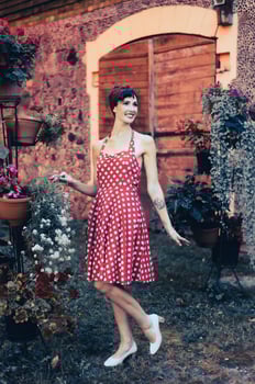 Retro style full body portrait of a beautiful woman posing in a red dress among blooming plants photo