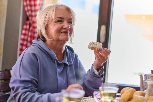 Elderly woman finds pure joy in the early morning as she savors a wholesome breakfast on the porch of her rustic cottage, embracing the serenity of nature that surrounds her photo