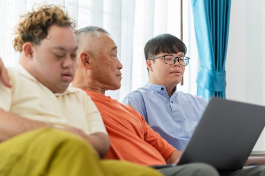 Grandfather and grandson using laptop doing a call in living room, Senior asian man having a good time sitting on couch at home with adult son photo