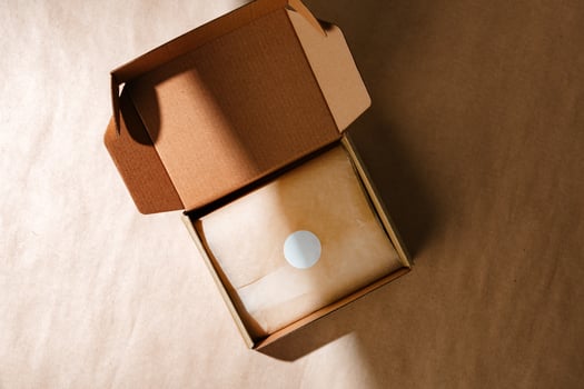 A sealed kraft box containing a wrapped item, positioned on a textured brown surface for an unboxing experience photo