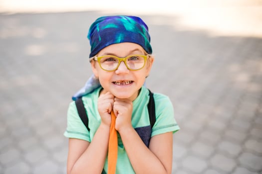 funny little boy in glasses, bandana, wearing a green t-shirt and denim shorts, having fun with a toy monkey photo