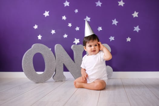 One year old baby boy celebrates birthday near silver letters ONE on blue background with stars photo