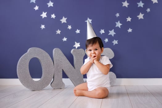 One year old baby boy celebrates birthday near silver letters ONE on blue background with stars photo