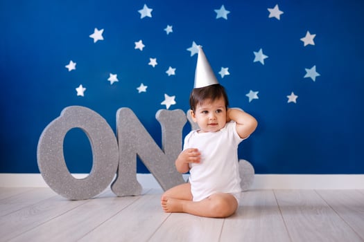 One year old baby boy in white t-shirt and silver hat celebrates birthday near silver letters ONE on blue background with stars photo