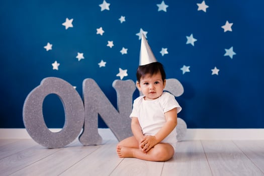 Baby boy of one year old sits on the floor on a blue background with stars and big silver letters one photo