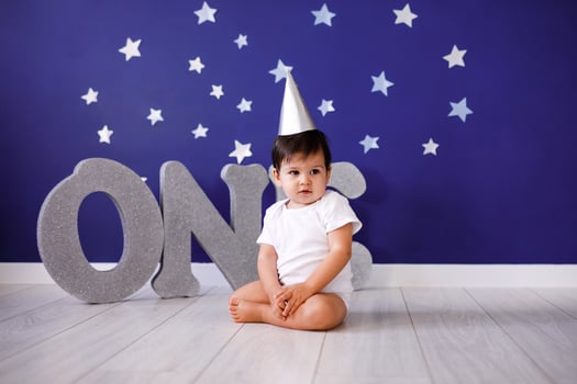 One year old baby boy celebrates birthday near silver letters ONE on blue background with stars photo