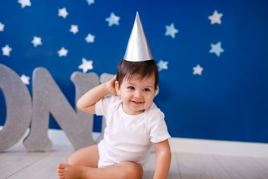 One year old baby boy celebrates birthday near silver letters ONE on blue background with stars photo