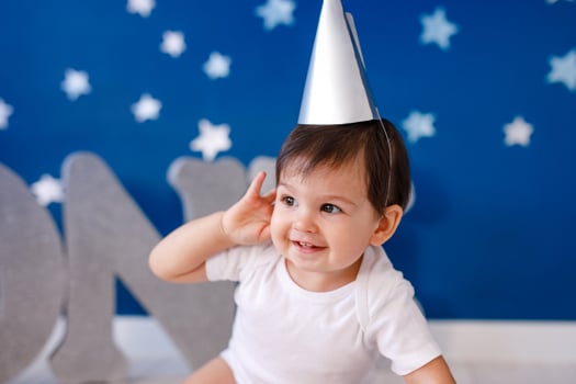 One year old baby boy in white t-shirt and silver hat celebrates birthday near silver letters ONE on purple background with stars photo