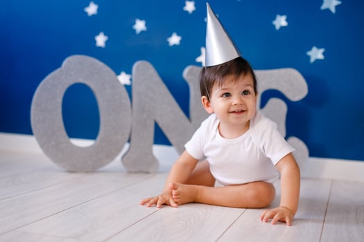 One year old baby boy in white t-shirt and silver hat celebrates birthday near silver letters ONE on purple background with stars photo