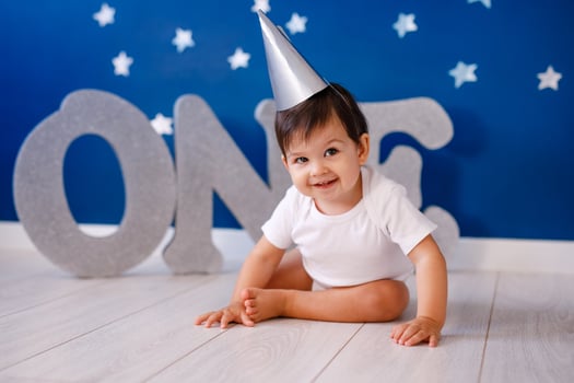 One year old baby boy celebrates birthday near silver letters ONE on blue background with stars photo